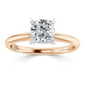 A cushion-cut diamond solitaire ring with a rose gold band and white gold prongs, shown on a white background.