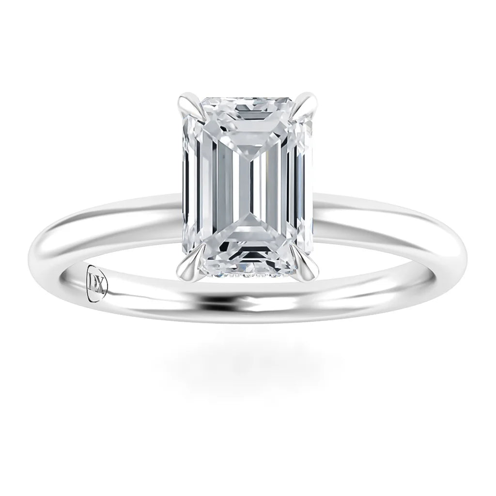 Emerald-cut diamond solitaire ring with a thin, polished white metal band on a white background.