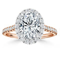 Oval diamond ring with halo and pavé diamonds on a rose gold band, set against a white background.