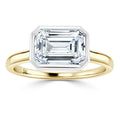 Gold band ring with a large emerald-cut diamond set in a geometric bezel setting, on a white background.