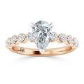 Rose gold ring with a pear-shaped diamond center and round side diamonds on the band.