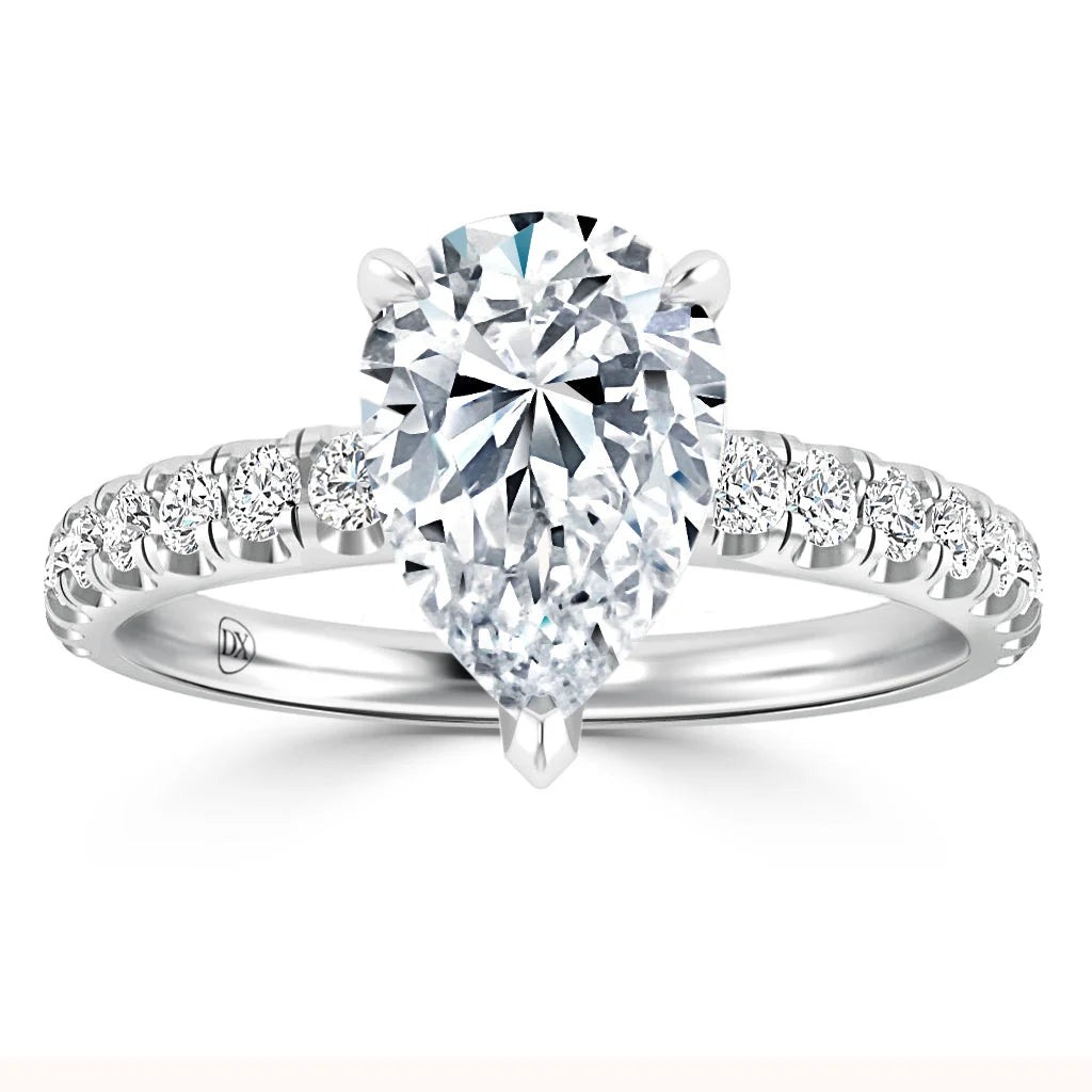 A pear-shaped diamond ring with a pavé diamond band set in white gold against a white background.