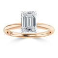 A rose gold ring with a large emerald-cut diamond solitaire set in a minimalist prong setting.