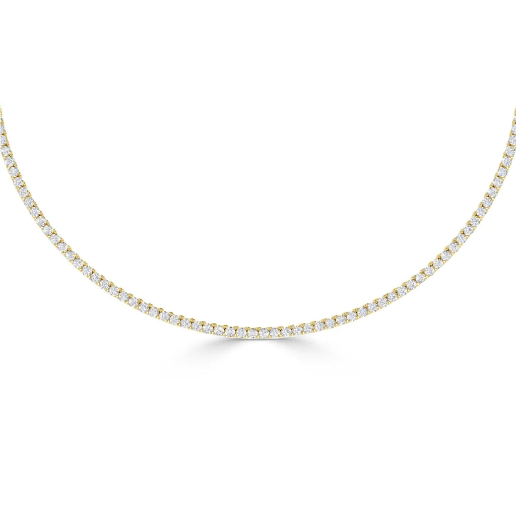 A thin gold tennis necklace with small, closely set white diamonds in a single row, shown on a white background.