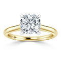A gold band ring with a cushion-cut diamond solitaire held by four prongs on a white background.