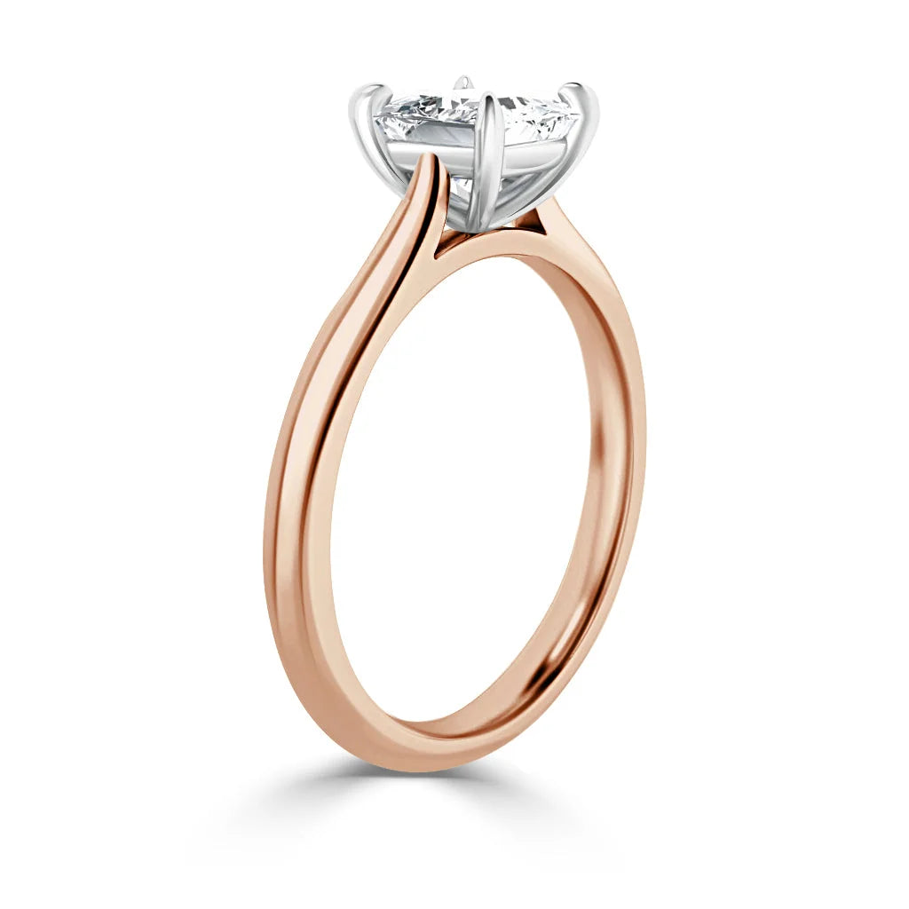 A rose gold ring with a round solitaire diamond in a white gold prong setting, shown from the side.