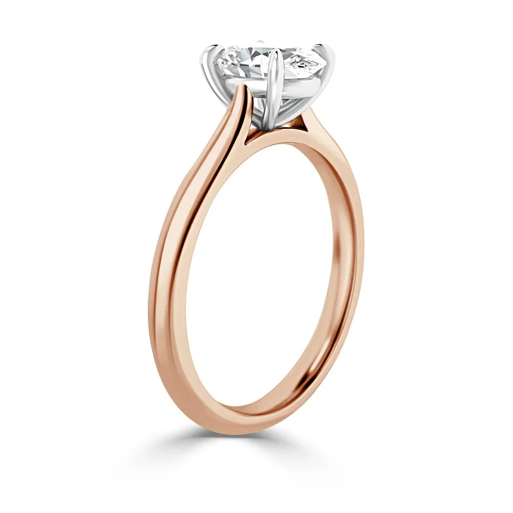 A rose gold solitaire ring with a round diamond held by a four-prong white gold setting, side view.