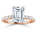 Emerald-cut diamond ring with rose gold band and round diamonds set along the band, on white background.