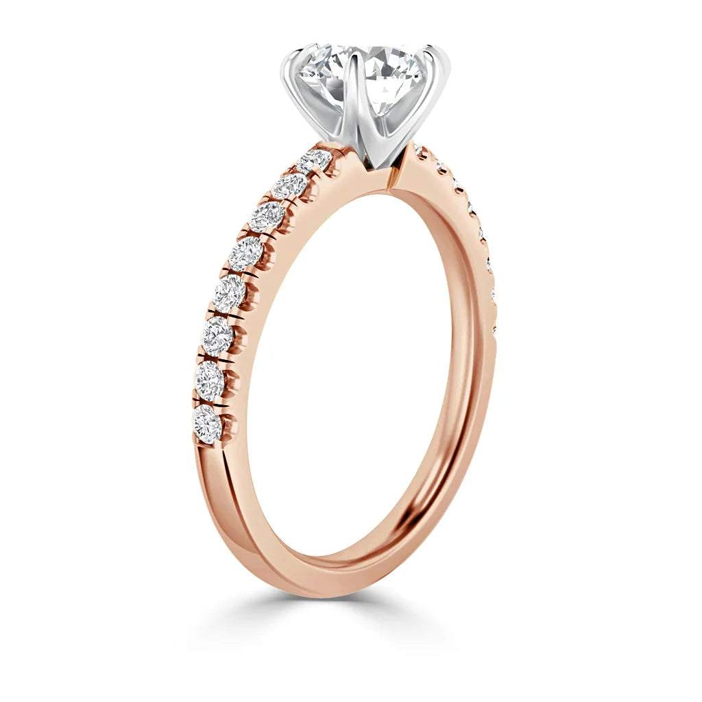 A rose gold ring with a round, raised diamond and small diamonds set along the thin band.
