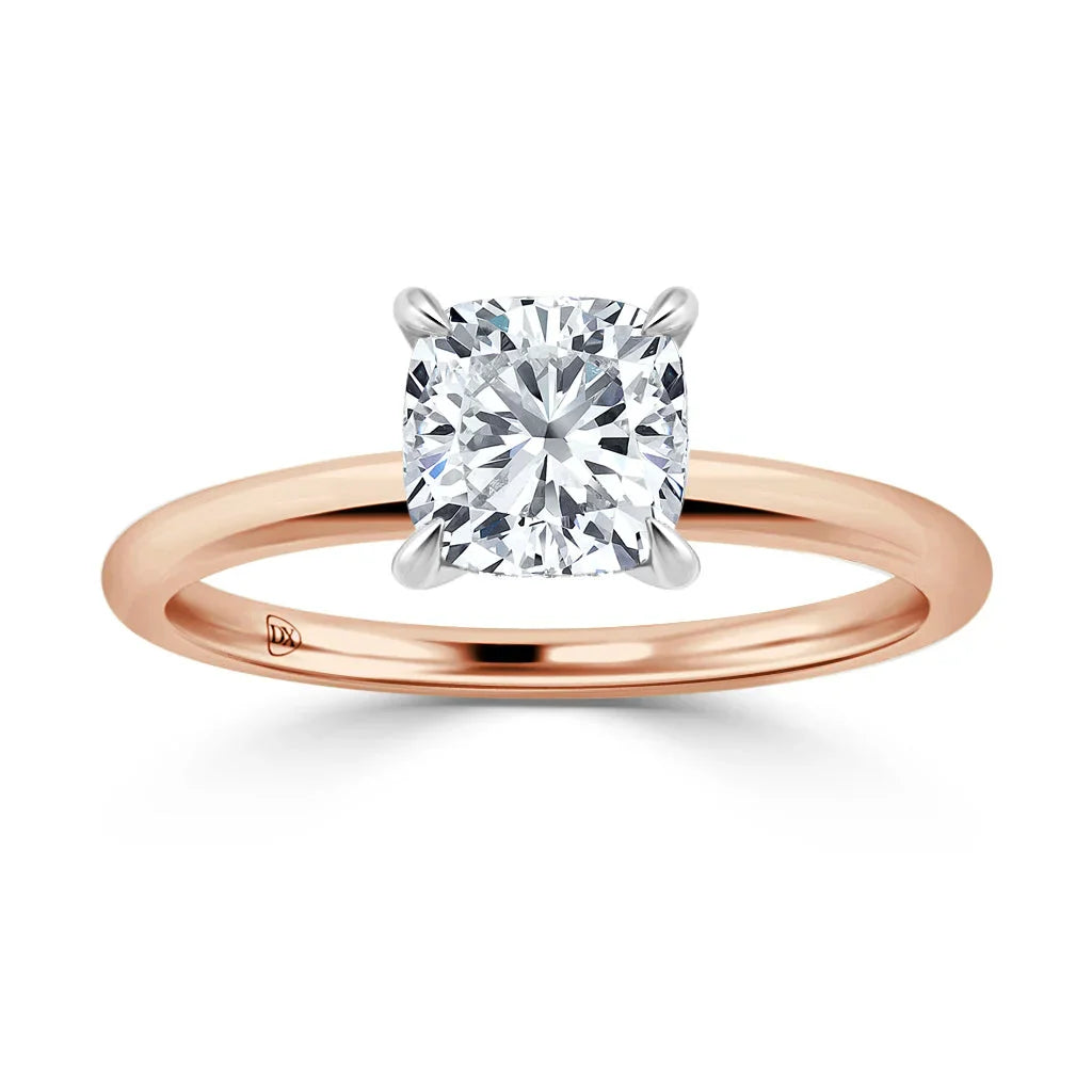Rose gold band solitaire ring with a cushion-cut diamond in a four-prong white gold setting, on a white background.