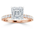 A rose gold ring with an Asscher-cut diamond center and round diamonds on the band, on a white background.