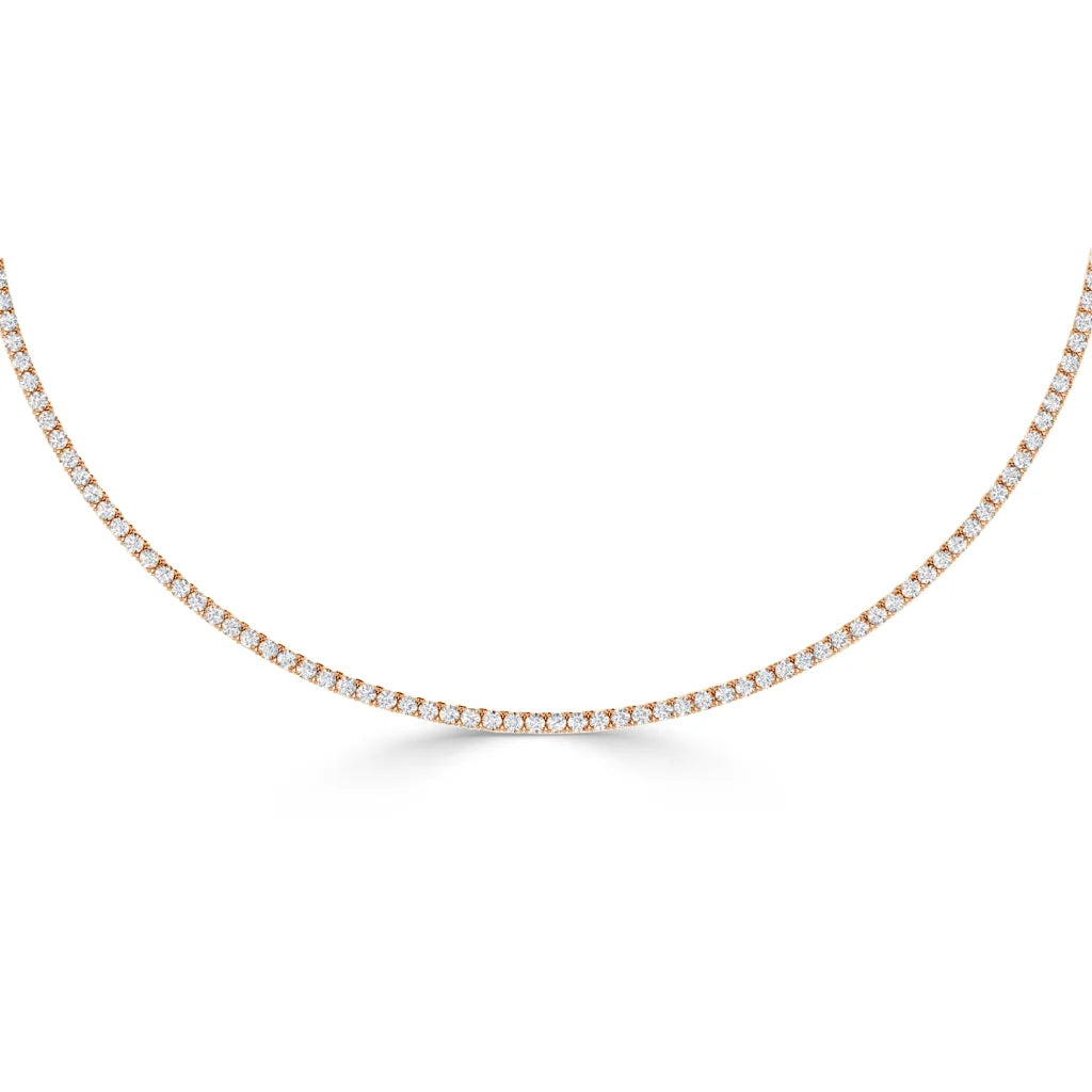 A thin, gold tennis necklace set with small, round diamonds, displayed on a plain white background.