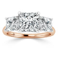 A rose gold ring with three princess-cut diamonds set in a row, center stone larger than the side stones.