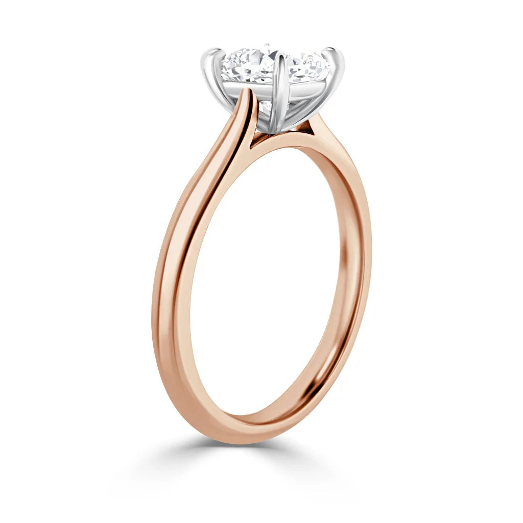 A rose gold engagement ring with a round diamond solitaire set in a white gold prong setting, shown side view.