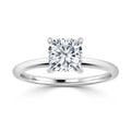 A cushion-cut diamond solitaire ring with a thin, polished white metal band on a white background.