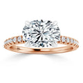 Rose gold ring with large oval diamond center stone and smaller diamonds set along the band, on white background.