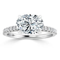Oval-cut diamond ring with side stones set on a thin pavé platinum band, shown on a white background.