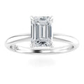 A solitaire emerald-cut diamond ring with a thin white gold band on a white background.