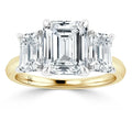 A gold ring with three emerald-cut diamonds, the center stone is larger than the two side stones.