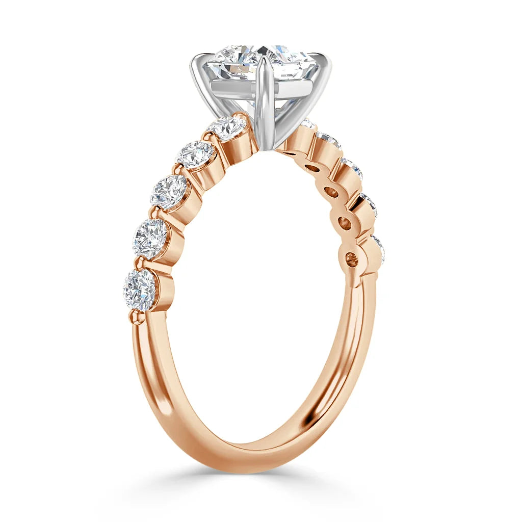 A rose gold ring with a large round diamond and smaller diamonds set along the band in a prong setting.