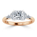A rose gold ring with a princess-cut center diamond and two marquise-cut diamonds on each side.
