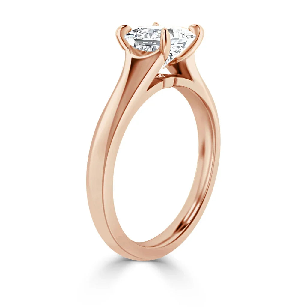 Rose gold solitaire engagement ring with a prong-set round diamond, shown from a side angle on a white background.