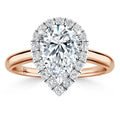 Pear-shaped diamond ring with halo of small diamonds on a rose gold band, shown against a white background.