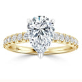 Gold ring with a large pear-shaped diamond center and smaller round diamonds on the band, on white background.