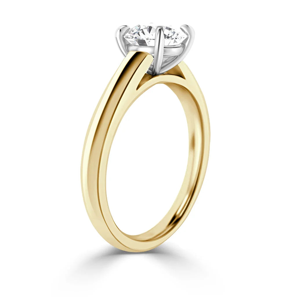 A gold solitaire ring with a round diamond set in a four-prong white gold setting, shown on a white background.