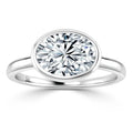 A silver ring with an oval, bezel-set, brilliant-cut diamond solitaire on a plain band.