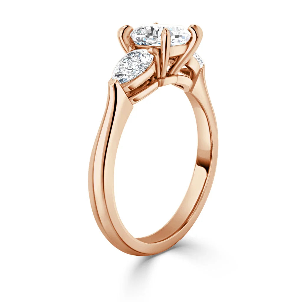 Rose gold ring with three oval-cut white diamonds in prong settings, shown from a side angle on a white background.