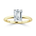 Gold band ring with an emerald-cut diamond solitaire set in four prongs against a white background.