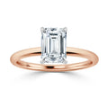 A rose gold band solitaire ring with an emerald-cut diamond in a four-prong setting, on a white background.