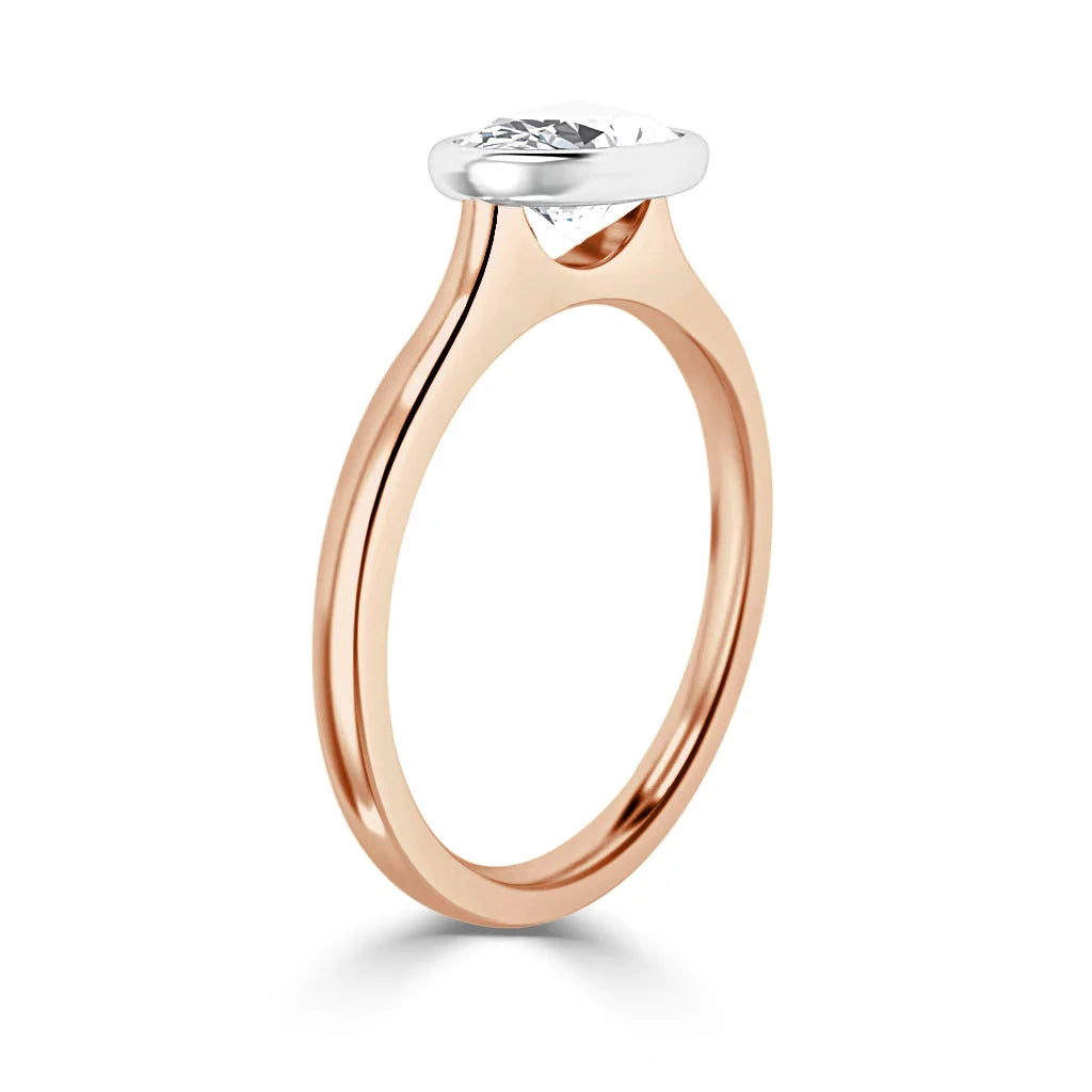 A rose gold ring with a bezel-set oval diamond in a white gold setting, shown on a white background.