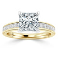 Princess-cut diamond ring with a gold band, side diamonds set into the band, and a four-prong setting.