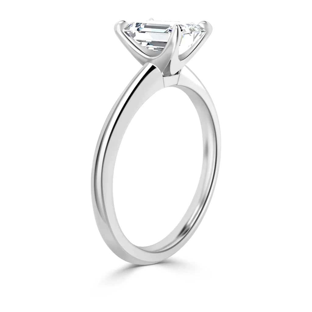 Silver solitaire ring with a large emerald-cut diamond in a prong setting on a plain band, side view.