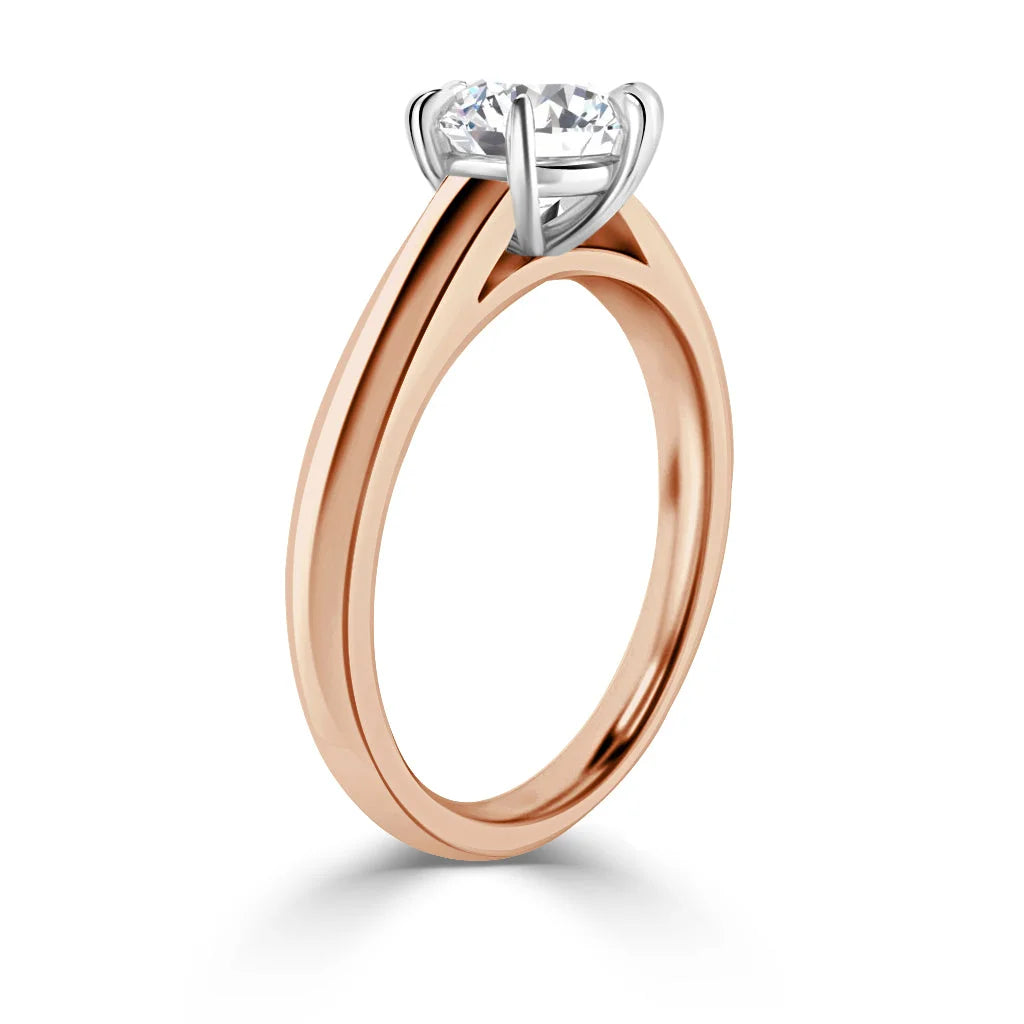 A rose gold ring with a round solitaire diamond in a white gold prong setting, shown from the side.