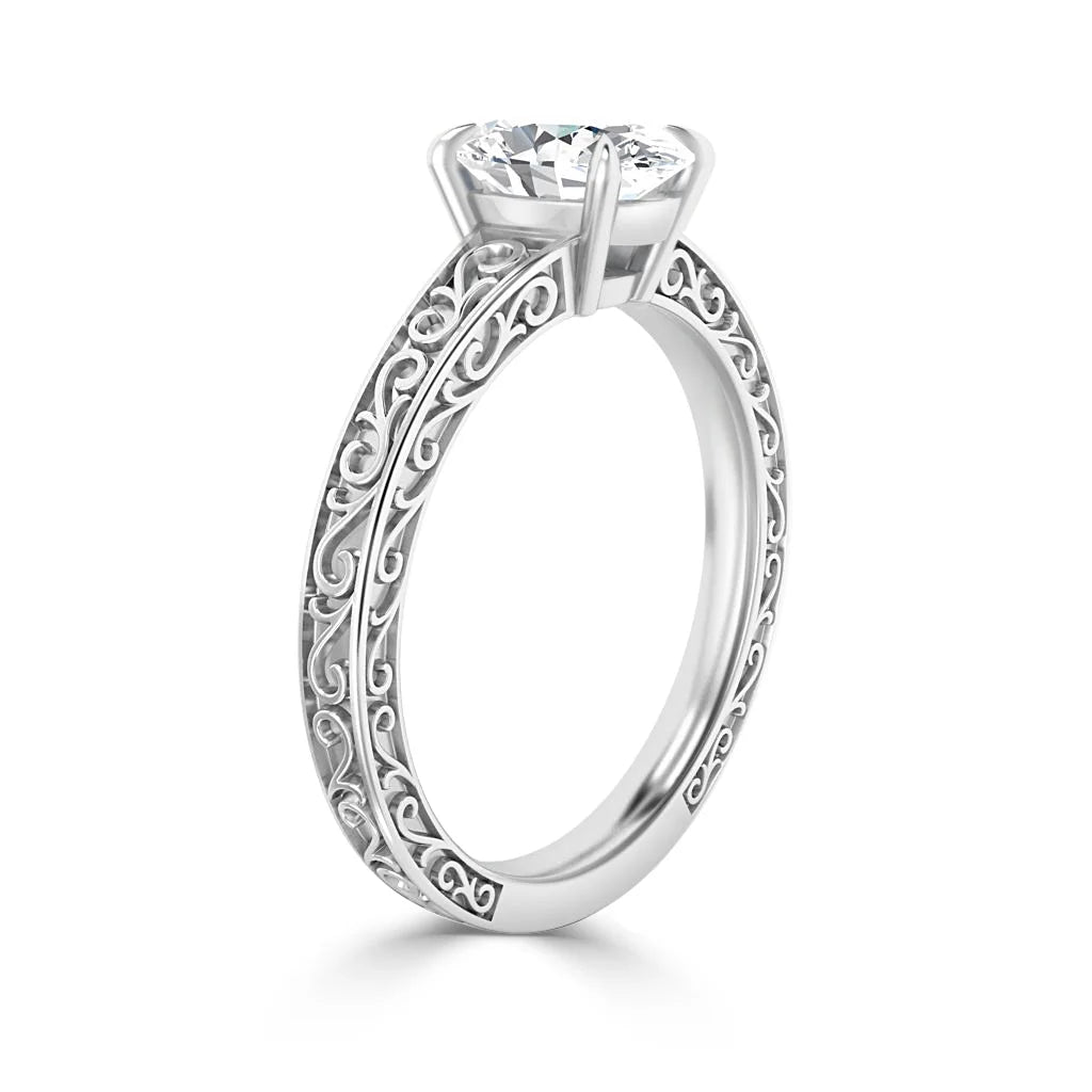 Silver ring with a round diamond solitaire and intricate scrollwork patterns along the band’s sides.