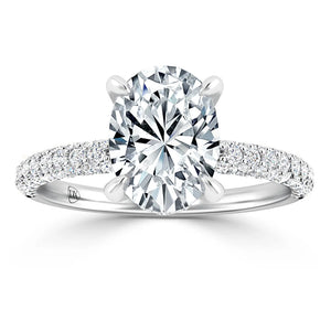 Oval-cut diamond ring with a pavé band and four prongs on a white background.
