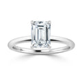 A solitaire emerald-cut diamond ring with a simple, thin silver band on a white background.