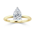 A pear-shaped diamond solitaire on a thin, polished yellow gold band against a white background.