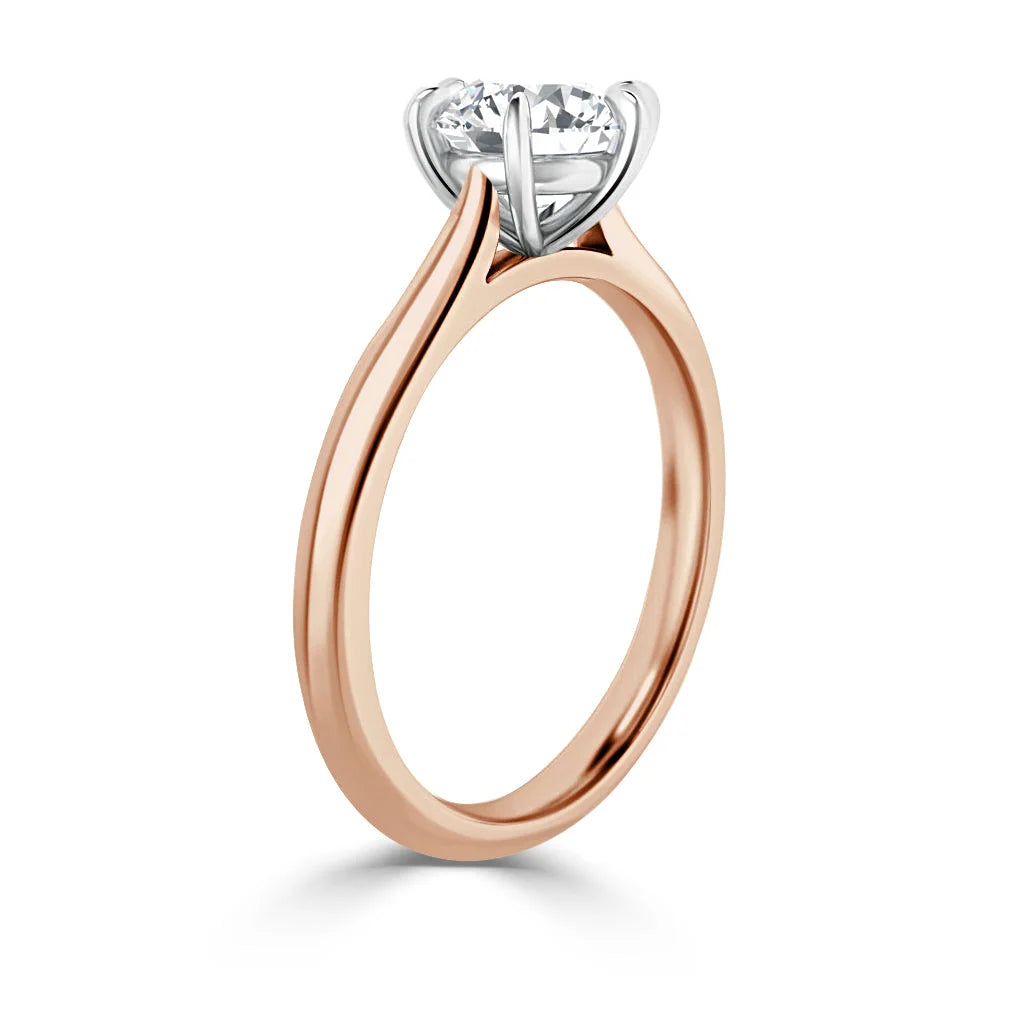 Rose gold solitaire ring with a round diamond set in a white gold prong setting, shown from the side.