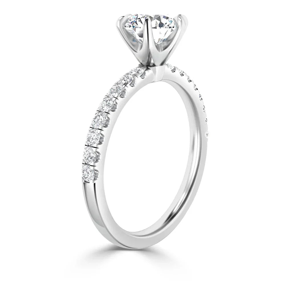White gold engagement ring with large round center diamond and smaller diamonds along the band, shown from the side.