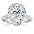 A pear-shaped diamond ring with a halo and band of round diamonds set in white metal.