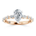 A pear-shaped diamond ring in rose gold with marquise and round side stones on a twisted band.