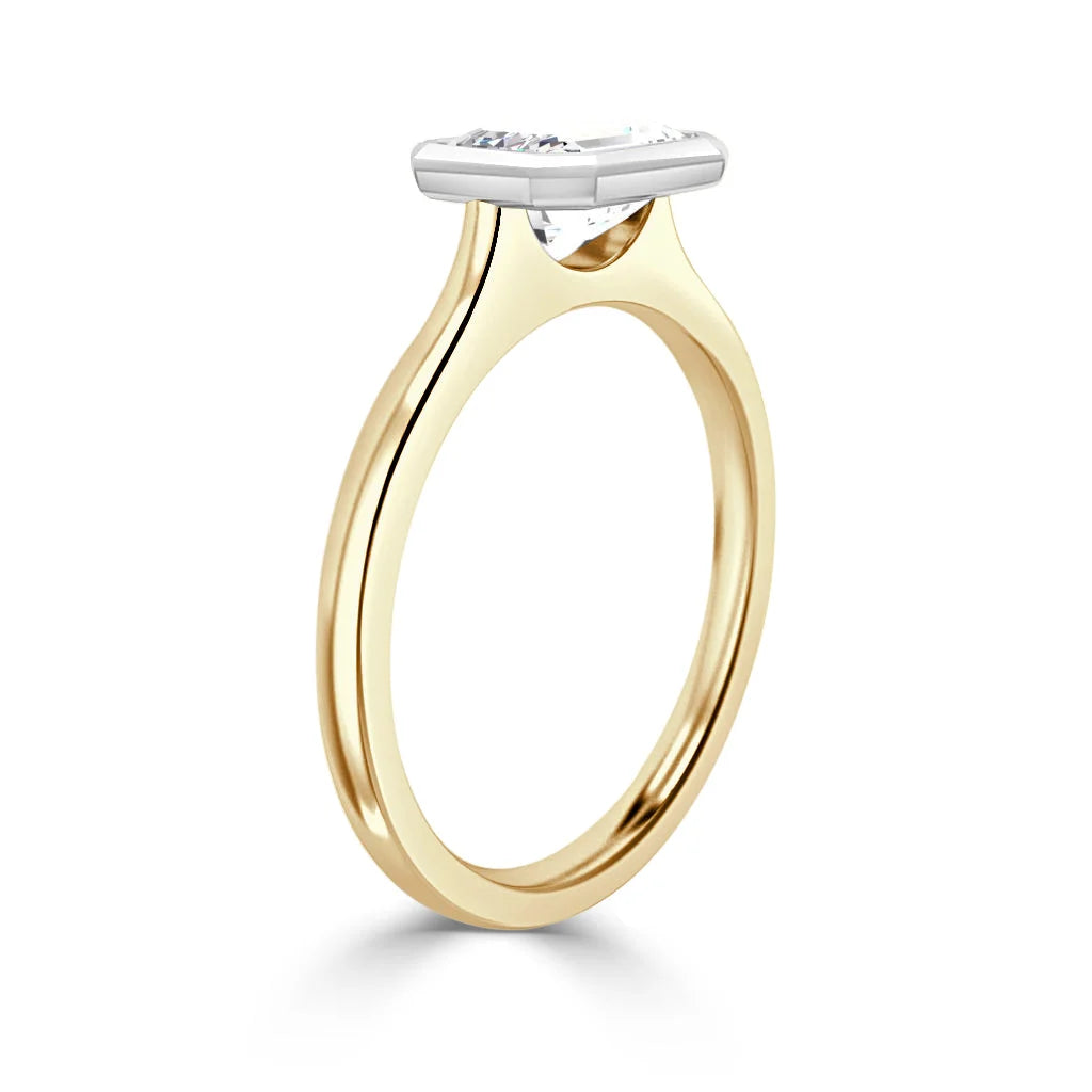 Gold ring with a thin band and a horizontally-set oval diamond in a white metal bezel setting, side view.