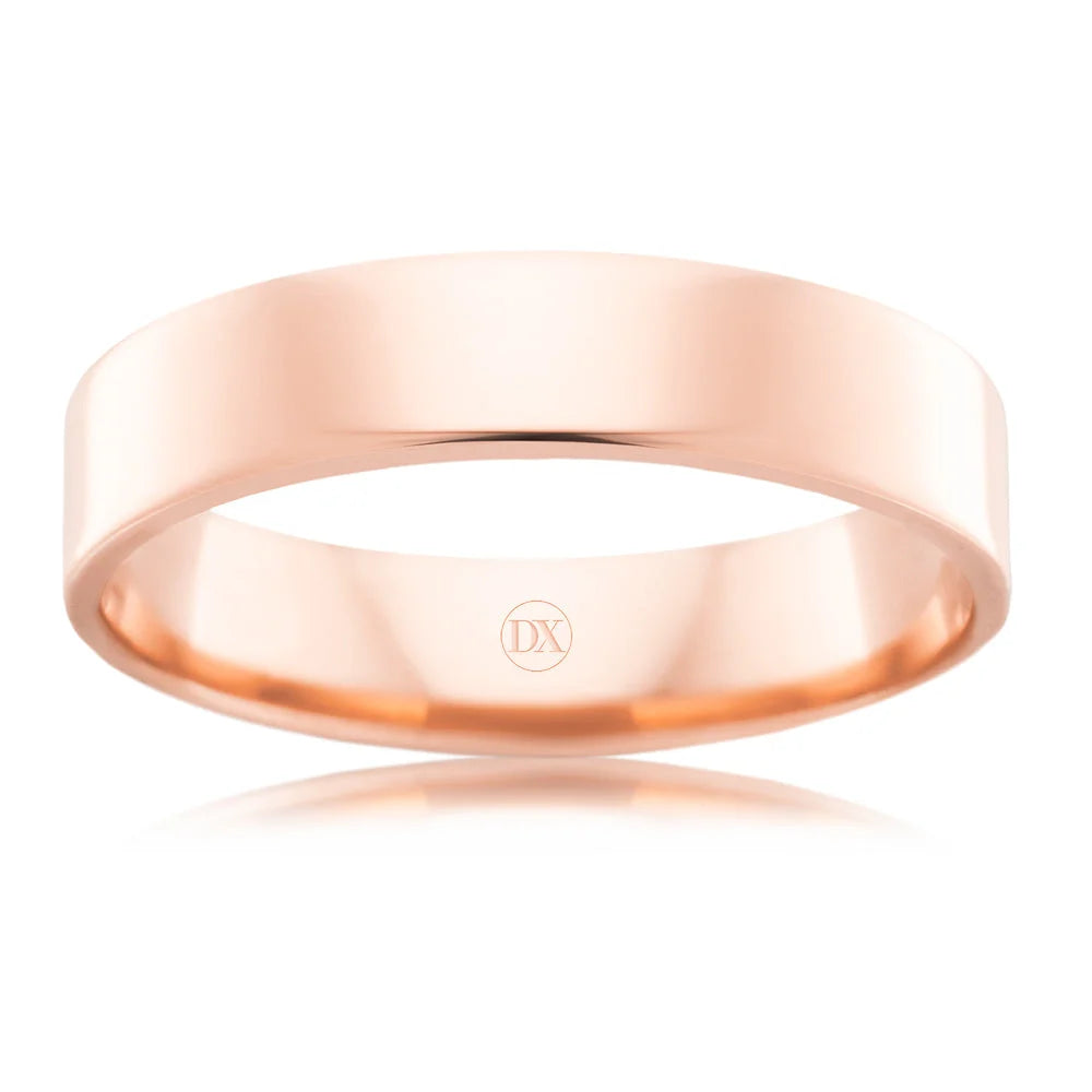 A plain, polished rose gold wedding band with a flat profile and a small engraved “DX” inside.